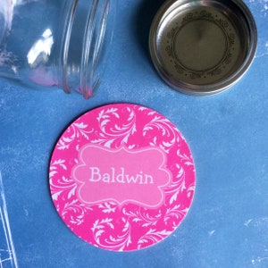 May include: Pink round label with a white floral pattern and a pink banner with the word "Baldwin" in white text.