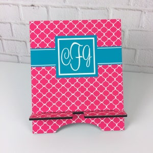 May include: A pink and white patterned phone stand with a teal blue band and a monogram of the letters "c f g" in white.