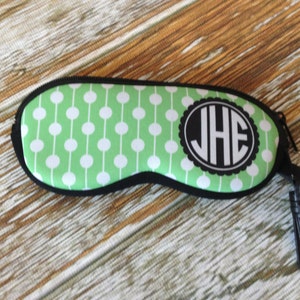 May include: Green and white polka dot eyeglass case with a black zipper and a black clip. The case has a white circle with the initials "JHE" in black.