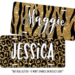 May include: Two license plates with personalized names. One plate has a gold glitter zebra print with the name "Maggie" in white script. The other plate has a gold glitter leopard print with the name "Jessica" in white block letters.