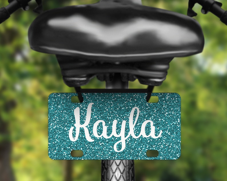 May include: A turquoise glitter bicycle license plate with the name "Kayla" in white cursive lettering.