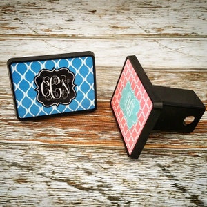 May include: Two personalized monogrammed hitch covers. One is blue with white trellis pattern and the monogram "CCN". The other is pink with white trellis pattern and the monogram "MB".