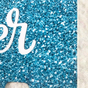 May include: A blue glitter phone case with a white "er" design.