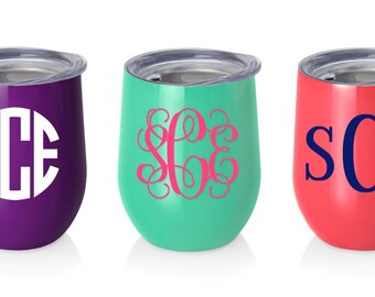 May include: Three stainless steel wine tumblers with different colored lids and monograms. The tumbler on the left is purple with a white monogram "SCE". The middle tumbler is teal with a pink monogram "SCE". The tumbler on the right is coral with a blue monogram "SCE".