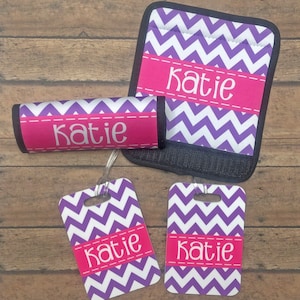 May include: Set of four luggage tags and a luggage handle cover with a purple and white chevron pattern. The tags and handle cover are personalized with the name "Katie" in pink.