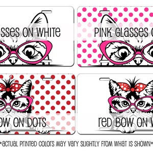May include: Four license plates with cat illustrations. The top left plate reads "PINK GLASSES ON WHITE" with a cat wearing pink glasses. The top right plate reads "PINK GLASSES ON DOTS" with a cat wearing pink glasses. The bottom left plate reads "red BOW ON DOTS" with a cat wearing pink glasses and a red bow. The bottom right plate reads "red BOW ON WHITE" with a cat wearing pink glasses and a red bow.