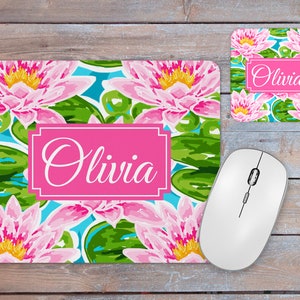 May include: A pink and green mousepad with a floral design and the name "Olivia" in a pink rectangle. The mousepad is on a wooden surface next to a white computer mouse and a matching pink and green coaster with the name "Olivia" in a pink rectangle.