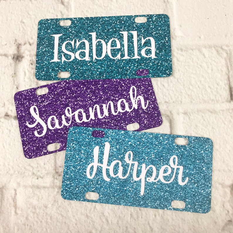 May include: Three glitter license plates with the names Isabella, Savannah, and Harper in white lettering.
