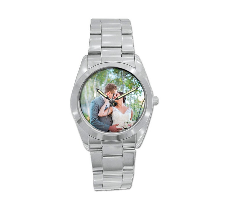 May include: A silver wristwatch with a round face featuring a photo of a couple kissing in a forest setting.