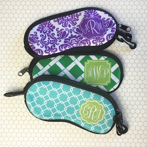 May include: Three eyeglass cases with different patterns and monograms. The top case is purple with a white damask pattern and the monogram "ARM". The middle case is green with a white diamond pattern and the monogram "HWP". The bottom case is blue with a white grid pattern and the monogram "GR".