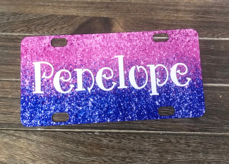 K&ouml;nnte beinhalten: Ein pinkfarbenes und blaues Glitzer-Kennzeichen mit dem Namen Penelope in wei&szlig;en Buchstaben.