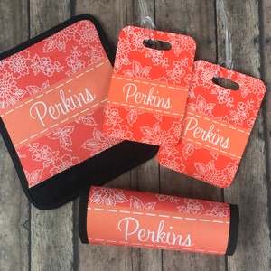 May include: Four luggage tags with a floral pattern in shades of orange and white. The tags have the name "Perkins" printed on them.