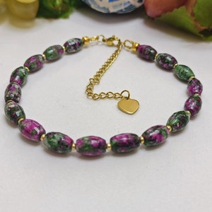 Op de afbeelding: Een armband van groene en roze edelstenen met een gouden hartbedel en een gouden verlengketting.
