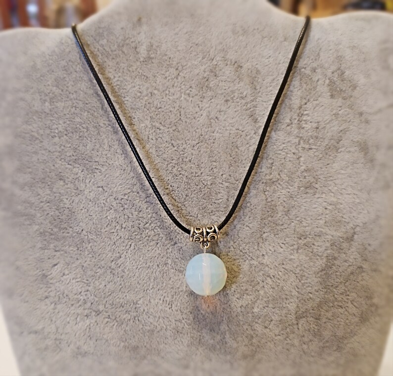 May include: A white opal pendant necklace on a black cord. The pendant is round and has a silver clasp.