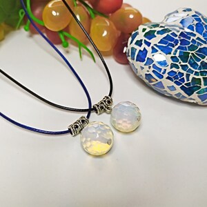 May include: Two necklaces with silver clasps and white opal pendants. The necklaces are on a white surface with a blue and green mosaic heart in the background.