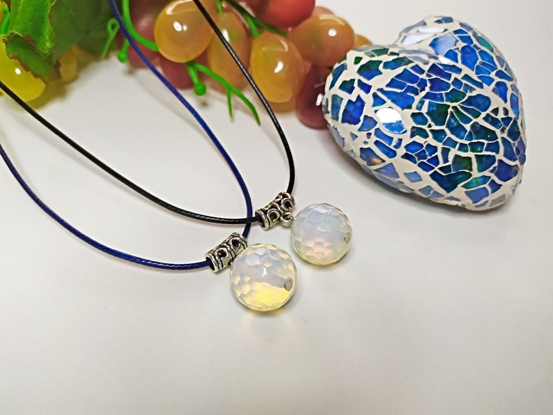 May include: Two necklaces with silver clasps and white opal pendants. The necklaces are on a white surface with a blue and green mosaic heart in the background.