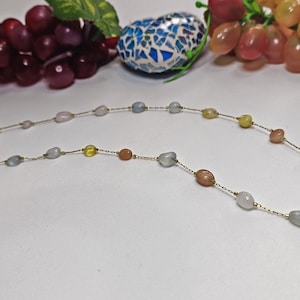 Könnte beinhalten: Eine zarte goldene Kettenkette mit abwechselnd pastellrosa, hellblauen und gelben ovalen Perlen.