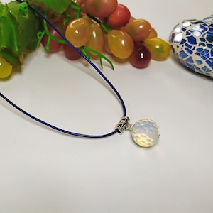 May include: A white opal pendant on a dark blue cord necklace. The pendant is round and has a textured surface.