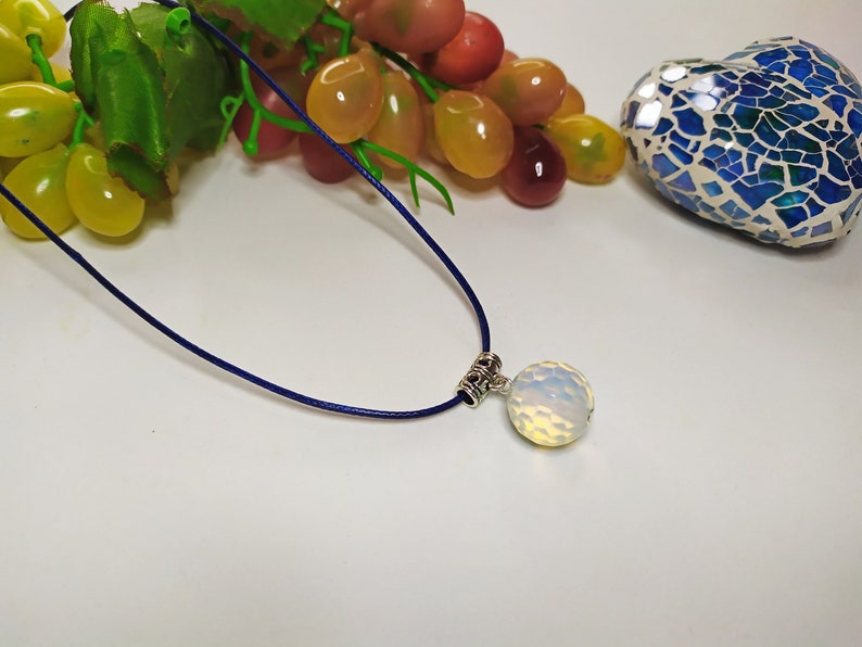 May include: A white opal pendant on a dark blue cord necklace. The pendant is round and has a textured surface.