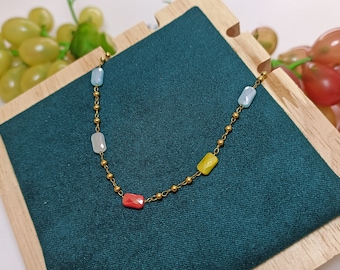 May include: A gold chain necklace with four rectangular gemstone beads. The beads are blue, white, yellow, and red.