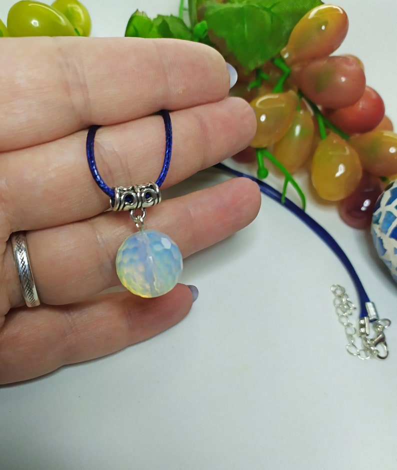 May include: A white opal gemstone pendant necklace with a silver chain and a blue cord. The pendant is round and has a faceted surface.