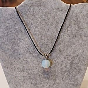 May include: A delicate necklace with a light blue opal pendant on a black cord. The pendant is round and has a silver clasp.