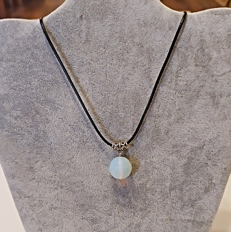 May include: A delicate necklace with a light blue opal pendant on a black cord. The pendant is round and has a silver clasp.