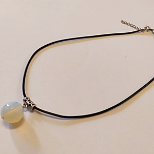 May include: A white opal pendant necklace with a black leather cord and silver clasp.