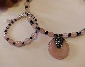 May include: A pink and black beaded necklace with a large pink pendant featuring a black rhinestone design.
