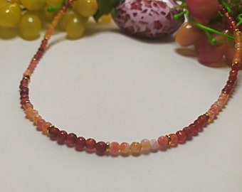 May include: A delicate necklace made of small, round beads in shades of red, orange, and yellow. The beads are strung on a thin gold chain.