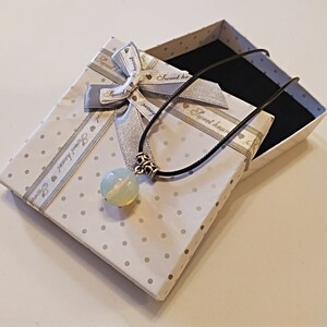 May include: A white gift box with a silver ribbon and a white opal pendant necklace with a black cord. The box has a white background with black polka dots and the text "Sweet heart" on the ribbon.