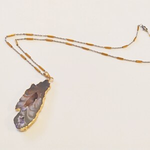 Peut inclure: Un collier en chaîne dorée avec un pendentif en agate brun et blanc. Le pendentif est une tranche d'agate naturelle avec une bordure dorée.