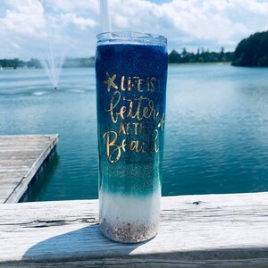 May include: A blue and green ombre glitter tumbler with a gold glitter starfish and the text "Life is better at the beach".