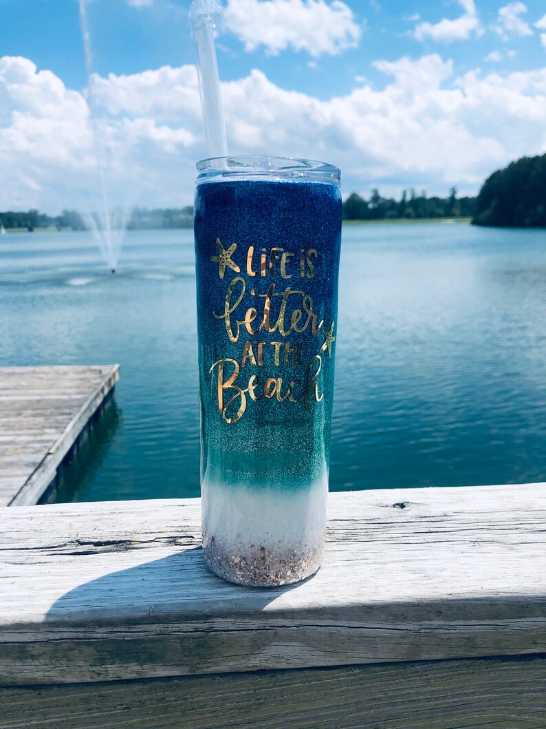 May include: A blue and green ombre glitter tumbler with a gold glitter starfish and the text "Life is better at the beach".