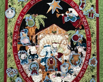 May include: A Christmas-themed quilt with a nativity scene in the center. The quilt is decorated with various ornaments, including a star, a stocking, a gift box, a bell, a candy cane, a tree, a wreath, a sheep, a cow, a donkey, and a manger. The quilt is surrounded by a green border with holly leaves and berries.