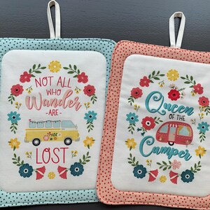 May include: Two white cotton pot holders with floral designs and a vintage camper van graphic. The left pot holder has the text "Not all who wander are lost". The right pot holder has the text "Queen of the Camper".