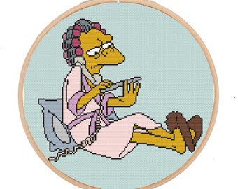 May include: Cross-stitch embroidery of a cartoon character in a pink robe, with curlers in her hair, talking on a phone and holding a nail clipper. The background is light blue.