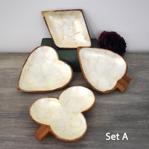 May include: A set of four wooden dishes with white mother-of-pearl inlay, shaped like playing card suits including a diamond, heart, spade, and club. Each dish features a smooth, light-colored interior and a dark wood rim. The text Set A is visible.