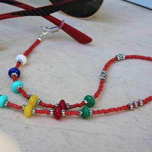 May include: Red beaded eyeglass chain with colorful beads, including white, blue, turquoise, yellow, red, and green. The chain has silver metal accents.
