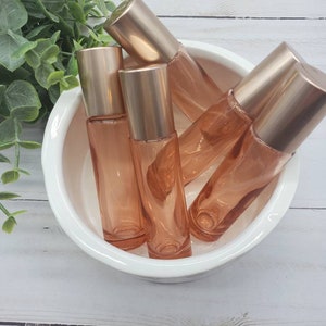 May include: Five amber glass roller bottles with gold lids in a white ceramic bowl. The bottles are filled with a clear liquid.