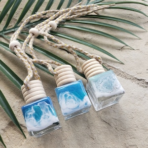 May include: Three glass car air fresheners with blue and white resin resembling ocean waves. Each air freshener has a wooden top and is attached to a twine string.
