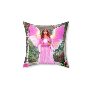 Puede incluir: Una almohada rosa con un diseño floral que presenta un ángel con alas sosteniendo una rosa. El ángel lleva un vestido rosa y una corona de flores.