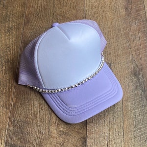 May include: A lavender trucker hat with a white front panel and a silver beaded trim around the brim.