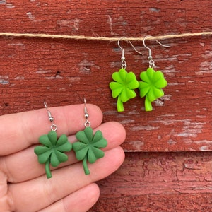 May include: A pair of green four-leaf clover earrings with silver hooks. The earrings are made of polymer clay and are about 1 inch in length.