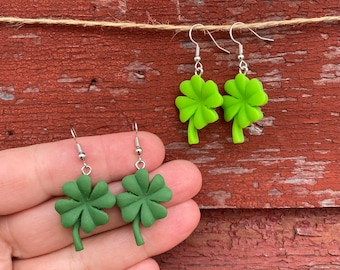 May include: A pair of green four-leaf clover earrings with silver hooks. The earrings are made of polymer clay and are about 1 inch in length.