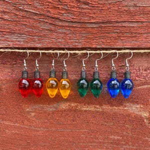 May include: Six pairs of dangle earrings featuring miniature light bulb charms in red, yellow, green, and blue. The earrings are hanging from a string.