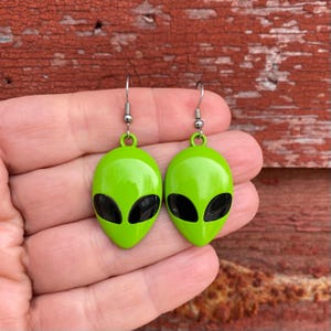 May include: Green alien head earrings with black eyes. The earrings are on a silver hook.