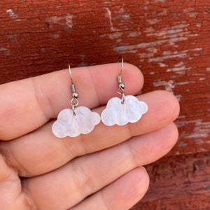 May include: A pair of silver dangle earrings with white cloud-shaped charms. The clouds have a marbled texture.