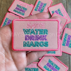 May include: Pink fabric patch with the text "SAVE WATER DRINK MARGS" in green, purple, and pink lettering.