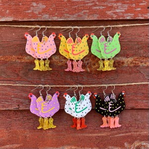 May include: Six pairs of colorful chicken earrings with glitter boots. Each pair features a different color and pattern, including pink, yellow, green, purple, white, and black.